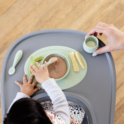 birds eye view of first food set with tiny bowl filled with food and tiny cup filled with milk with mom holding 