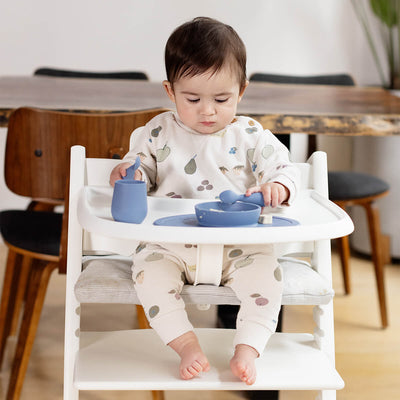 baby sittiing and holding two tiny spoons on both hands while one spoon placed on tiny bowl 