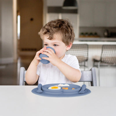 toddler sitting and drinking from tiny cup and food is placed in mini feeding set 