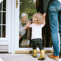 grandma by sliding glass door closed with child outside raising hand to match grandma