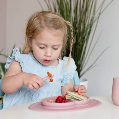 toddler sitting and eating food from mini feeding set 