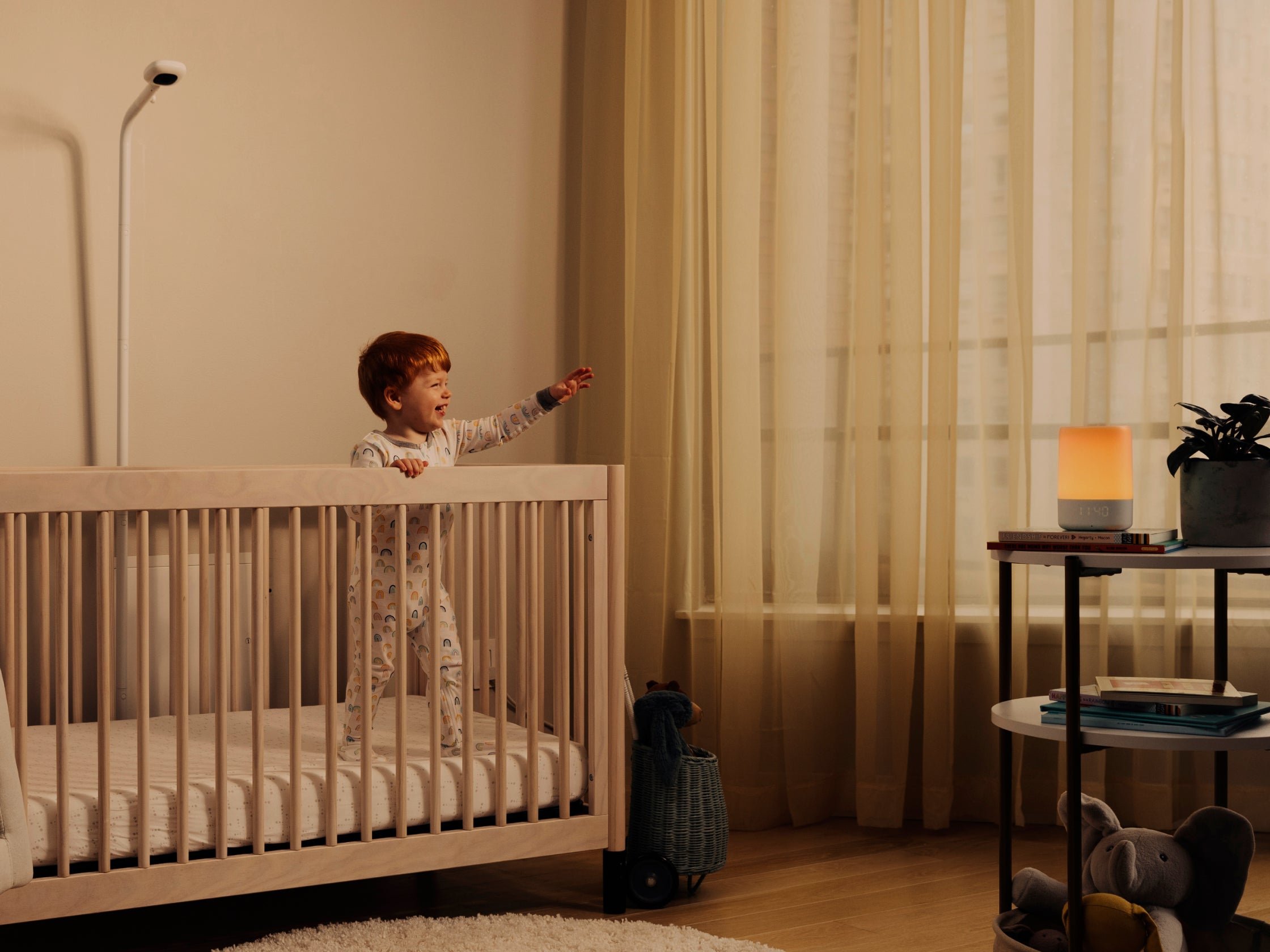 Baby smiling inside the crib while looking at sound + light and pro camera with floor stand looking down at crib