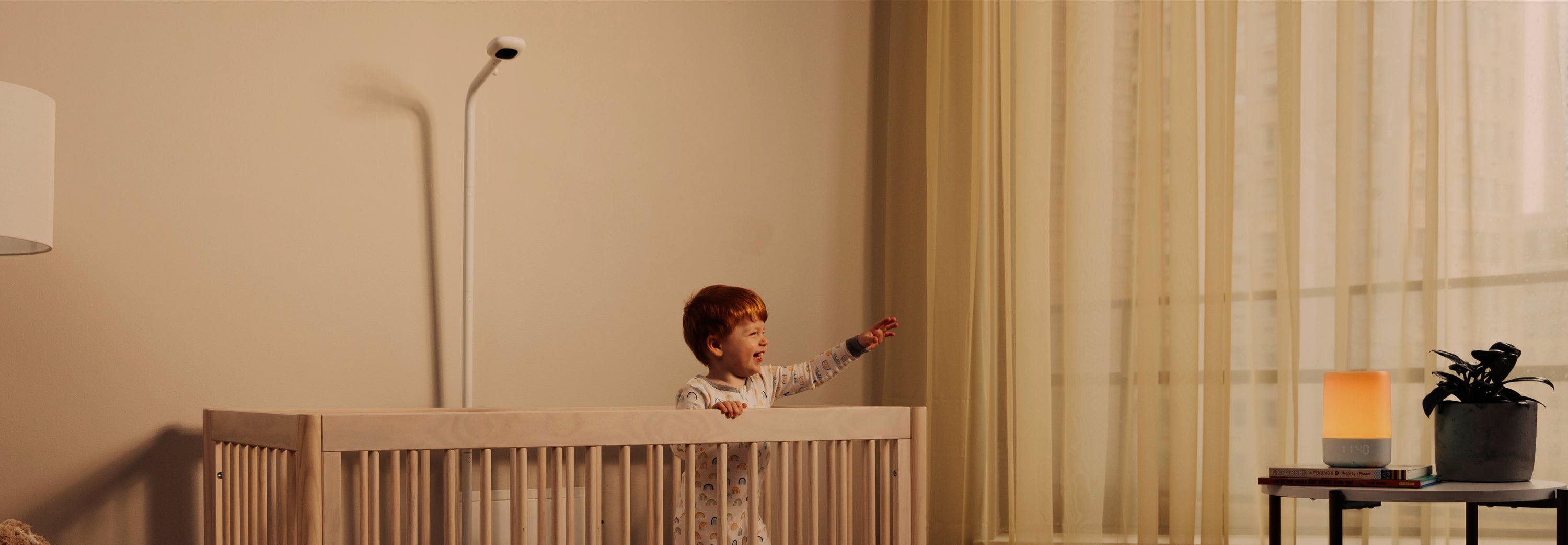 Baby smiling inside the crib while looking at sound + light and pro camera with floor stand looking down at crib