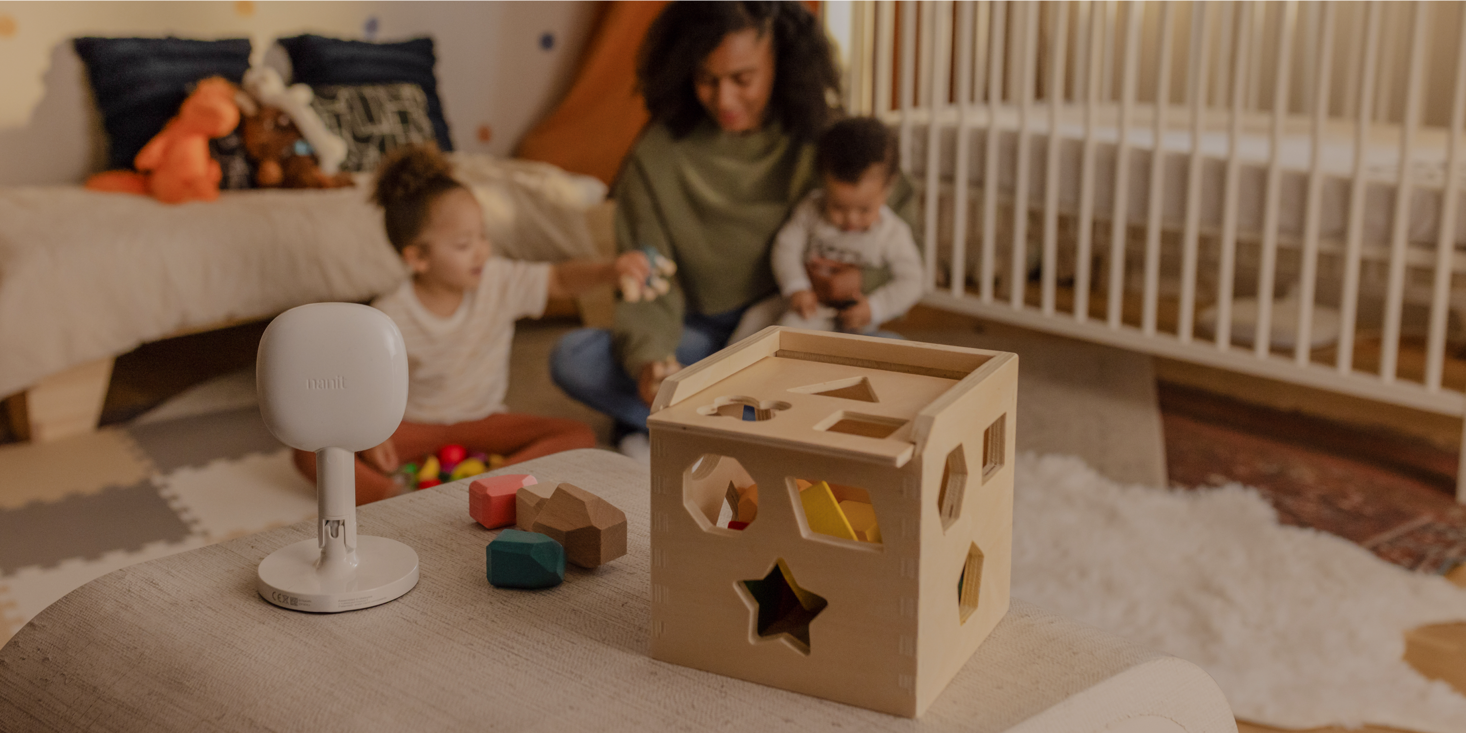 mom playing with kids while nanit baby monitor + flex stand monitors with blocks next to it