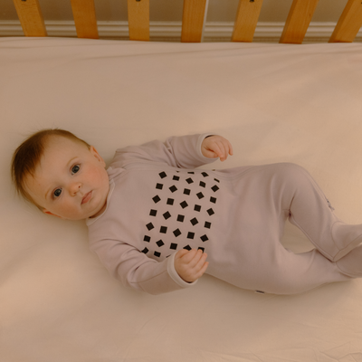 baby laying in crib in lilac pajamas 